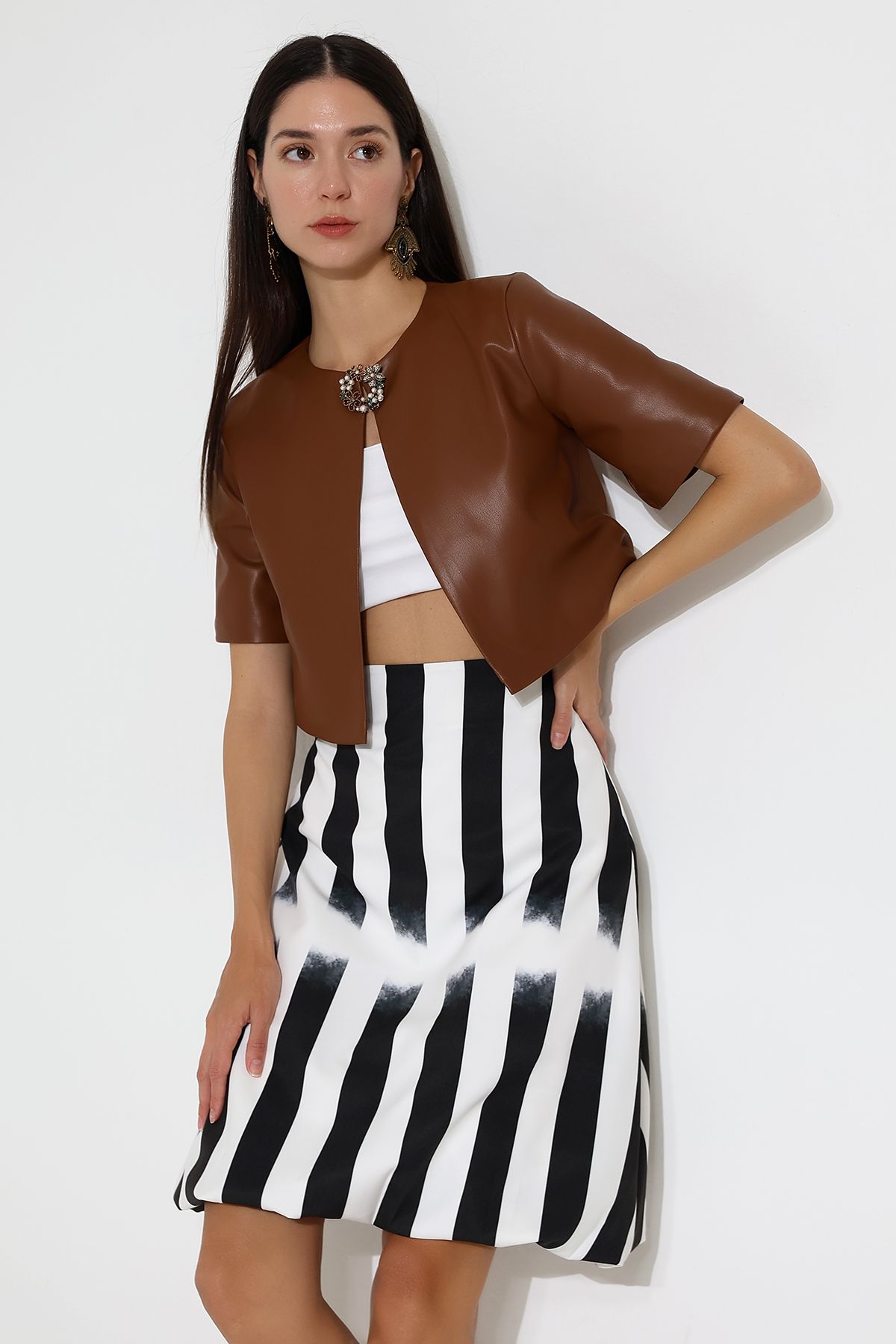 Model in striped skirt and tan leather short sleeved jacket standing