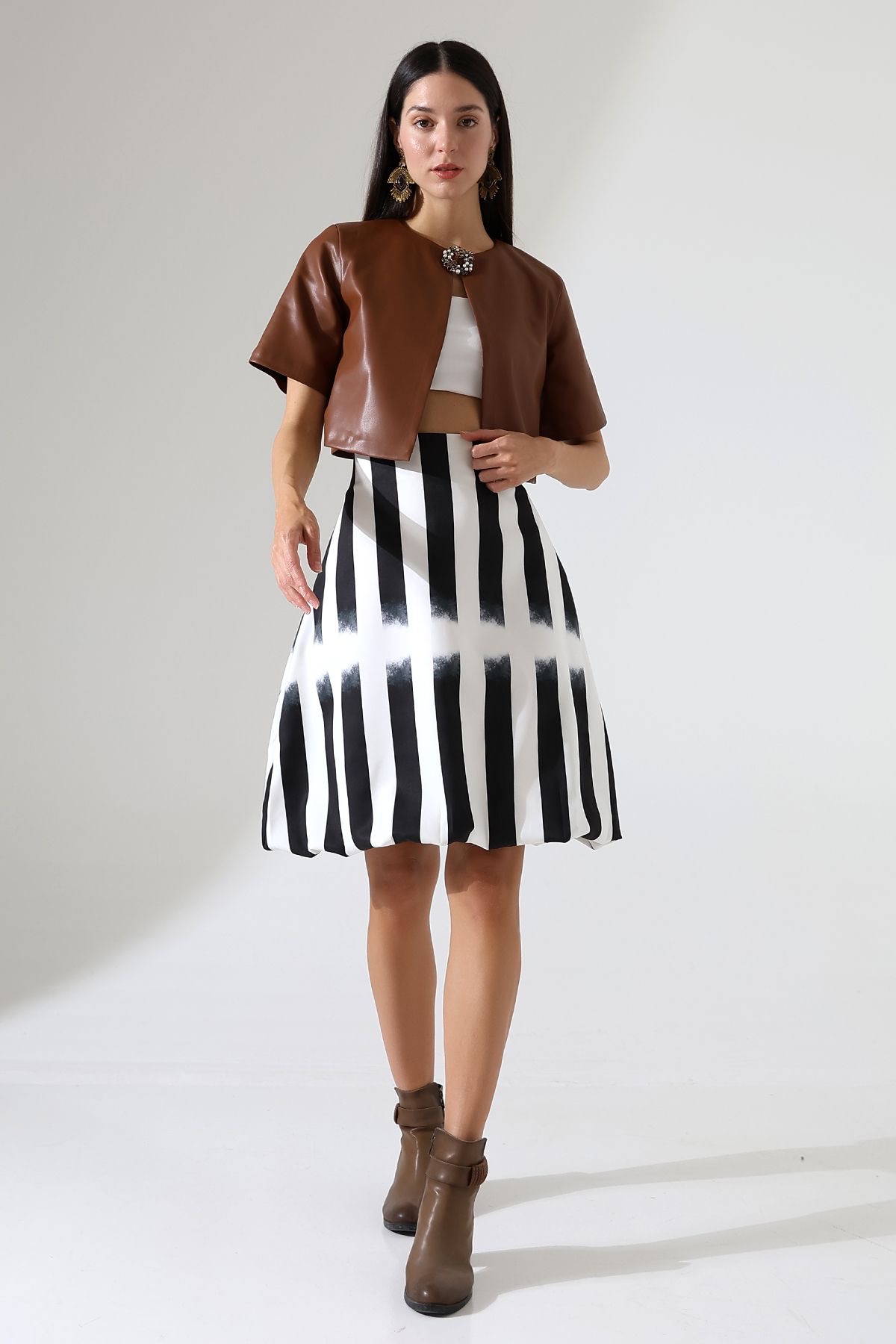 Full view of  model in striped skirt and tan leather short sleeved jacket 