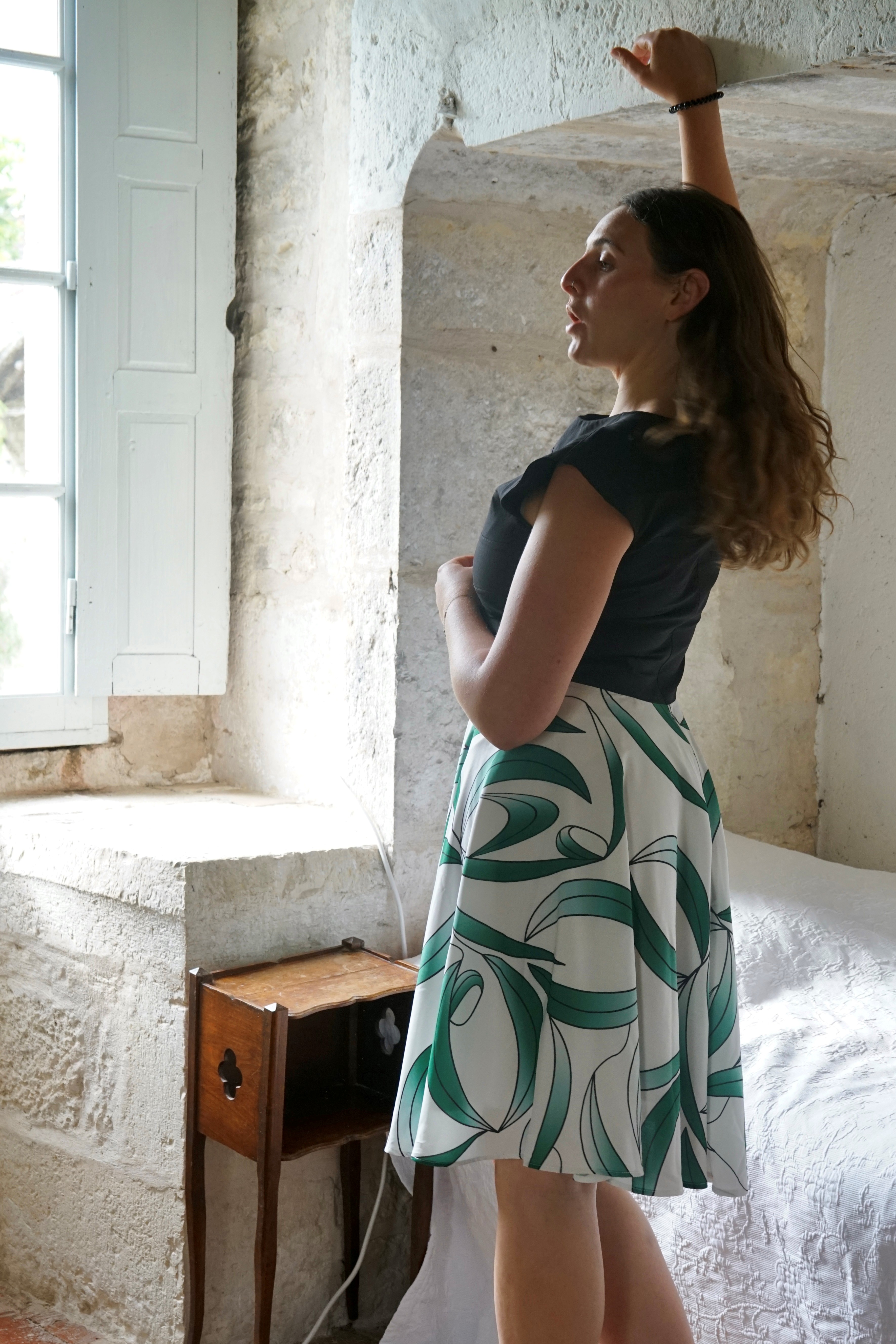 Back view of model in black topped dress with white and leaf green patterned skirt