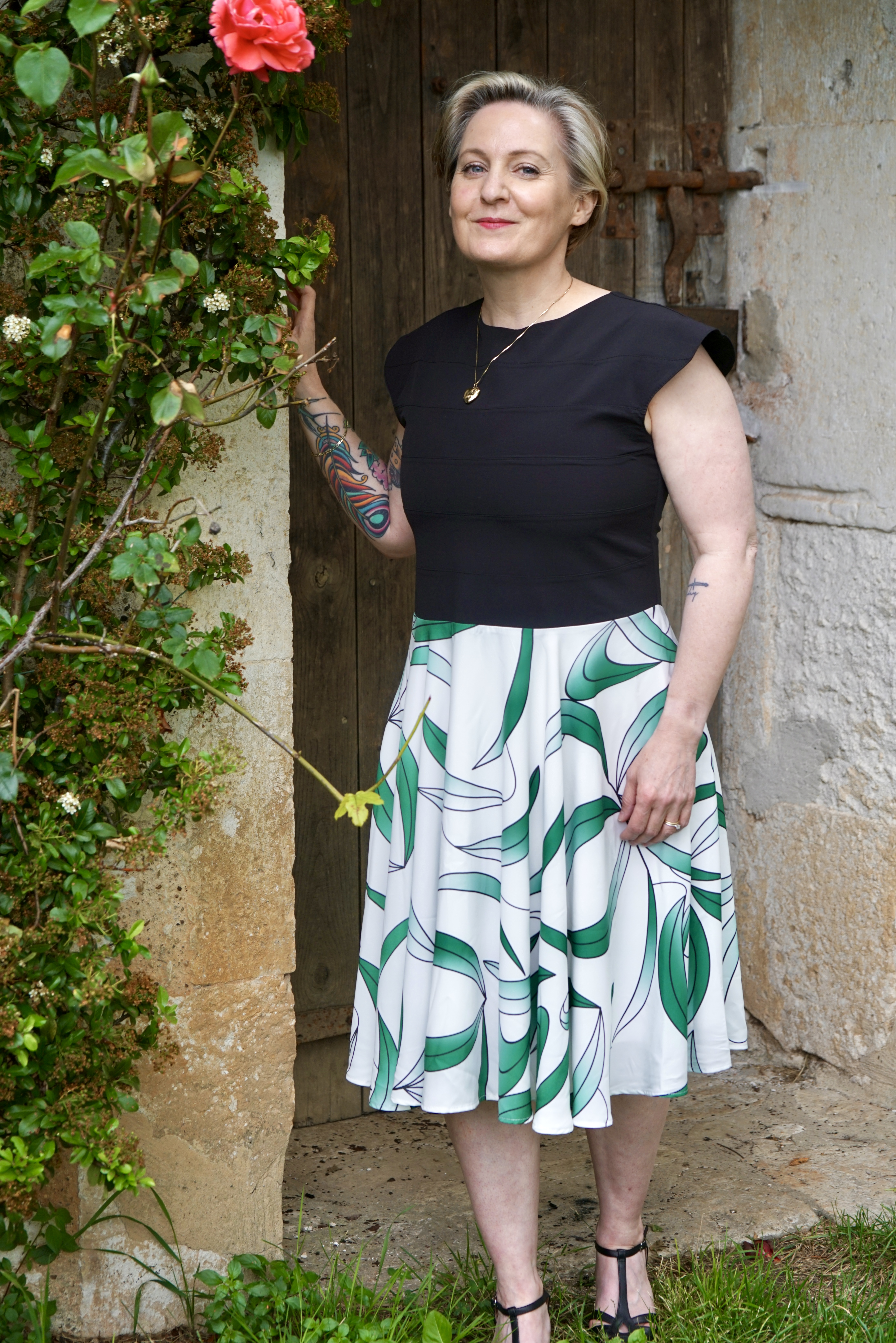 Model wearing  black topped dress with white and leaf green patterned skirt outside 